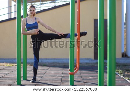 Pretty teenage girl making fitness exercises at stadium outdoors. Young woman is stretching her legs before running.
