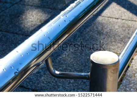 stainless steel pipe double handrail detail with rain drops and shadows. large blurry concrete tile paving in the background. modern construction materials concept.