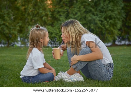 Beautiful mother and her little baby are playing outdoors in the park. Mom and daughter are resting in the park together. Lifestyle happy portrait, mom and daughter drink cocoa in the park.