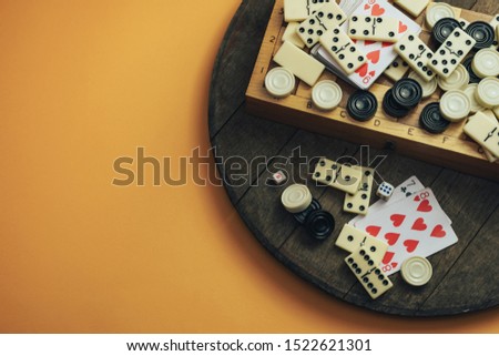 Various board games chess board, playing cards, dominoes on a old wooden table orange background.
