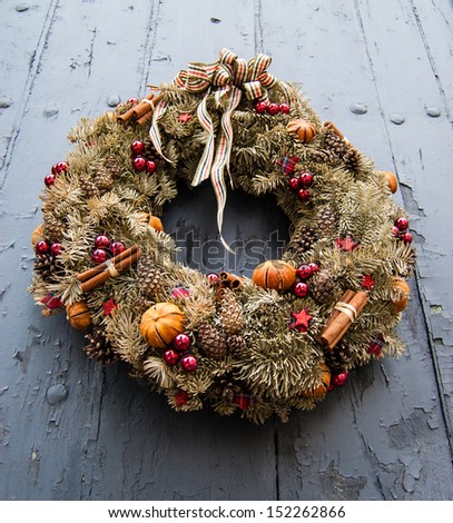 Vintage Christmas wreath with cinnamon sticks, dry oranges, red balls and stars on the grungy wooden door.