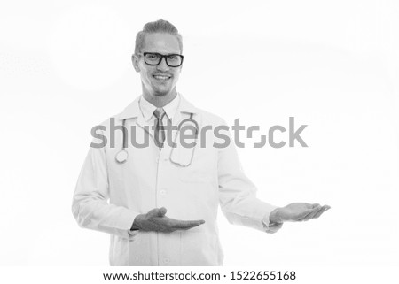 Studio shot of young happy man doctor smiling and showing something