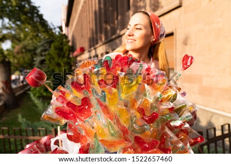 Girl holding a lollipop. Beautiful happy blond girl in the street. Young woman eating a piece of candy. 