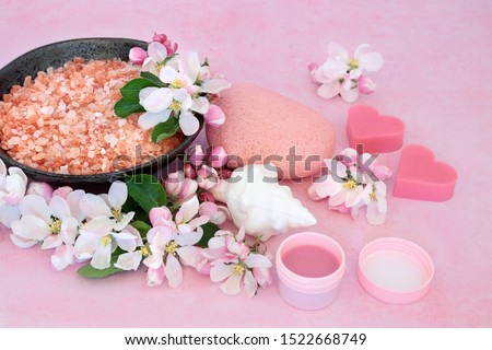 Skin care beauty treatment with exfoliation mineral salts, cleansing products and apple blossom flowers on pink background.