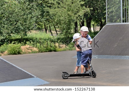 Two young brothers fighting over a toy scooter in a skate park having a tussle as to who will ride it next