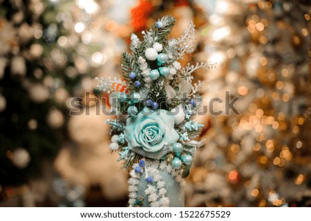 Vase with christmas decor composition of blue flowers, toys, fir-tree branches in the blurred background of winter decoration