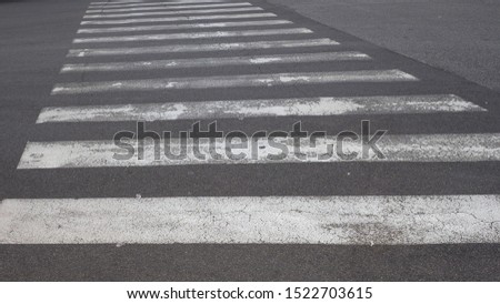 White pedestrian crossing or crosswalk lines on black asphalt, close up. Zebra crossing is place designated for pedestrians to cross most safely across a road, street or avenue.