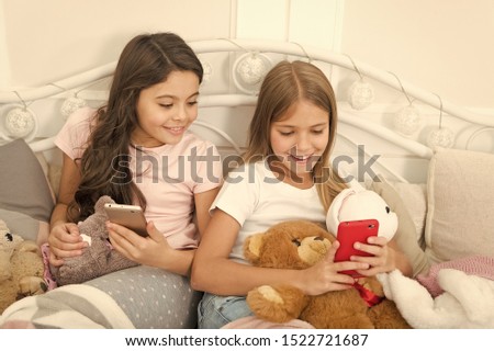 Sharing great pictures. Merry Christmas and Happy New Year greetings. Little girls use smartphone in bed. Happy little children with mobile phone. Ordering gifts for Christmas and New Year by phone.