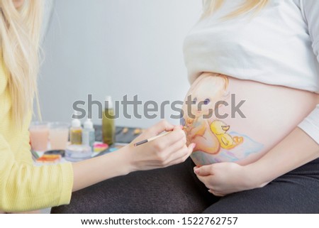 Makeup artist paints a child on the belly of a pregnant young woman