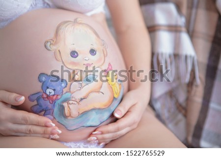 Cute drawing on the stomach of a pregnant woman in the form of a cheerful baby