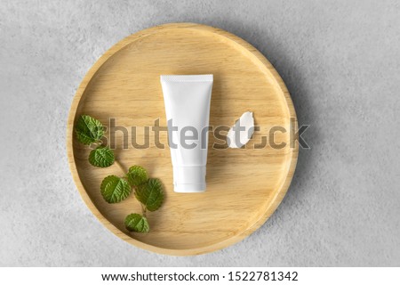 Top view of Organic gentle skincare white tube with mint leaves and rich moisture butter cream smear on a wooden plate. Royalty-Free Stock Photo #1522781342