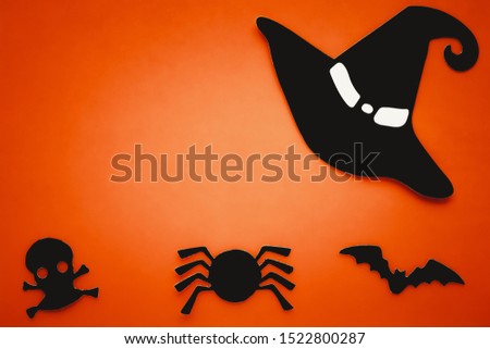 Orange background with black silhouette of spider, bat, skull, witch hat. Halloween card, paper composition. Abstract art. Invitation on bright orange backdrop, text space.