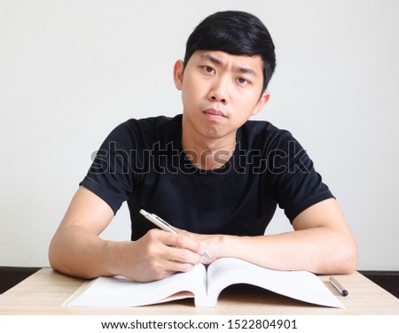 Young man with pen confused face and look at camera with the book on the desk on white isolated,Homework concept
