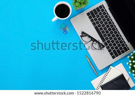 Top view desk,Modern office desk Workspace with laptop computer, coffee cup, glasses,notebook and office supplies for Working background concept,Blue glass table top.
