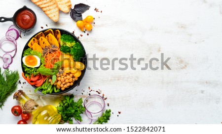 Buddha bowl: pumpkin, broccoli, egg, tomatoes, carrots, paprika in a black plate on a white wooden background. Top view. Free space for your text.