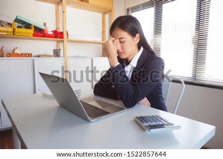 Young Asian woman feeling tired in the office after working hard in front of her laptop. Getting a headache or migraines with high tension Feeling painful with her eyesight with blurred vision concept