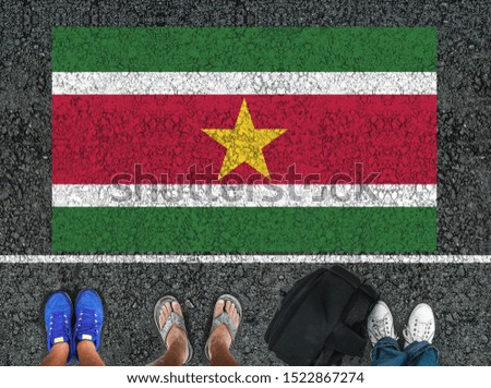 people legs are standing on asphalt road next to flag of Suriname and border