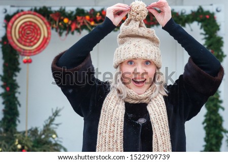 Happy beautiful funny young woman in knitted hat on  background of New Year decorations on the street. Christmas