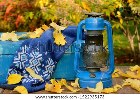 Autumn decoration with an old lamp, a box and a scarf with fallen leaves in the garden.