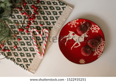 Christmas and new year flat lay. Red deer plate and sugar apples, candy cane and red berries on beige background