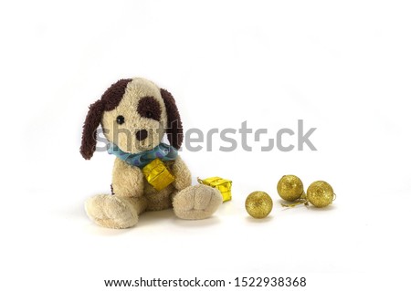 a toy dog holds in his paws a gift in golden paper, next to it are golden balls