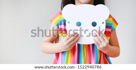 Close up little girl holding blank white animal paper mask on her chest on white background. Idea and concept for kid dressed up playing animal face.