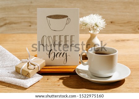 Mug with coffee and a vase of flowers on a wooden table. Greeting card
