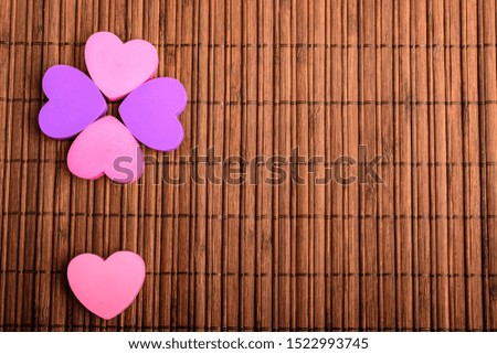 Five pink and mauve hearts on a brown bamboo table decoration, top view with space for text on the right side, selective focus

