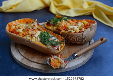 Two halves of pumpkin baked with vegetables on a wooden plate on a dark background, close-up.