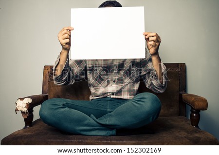 Man on old sofa holding a white sign