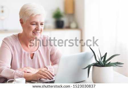 Smiling senior business woman looking at laptop, working from home, panorama with empty space