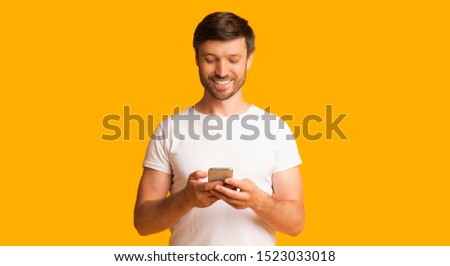 Mobile App. Happy Man Using Cellphone Standing Over Yellow Studio Background. Panorama With Copy Space