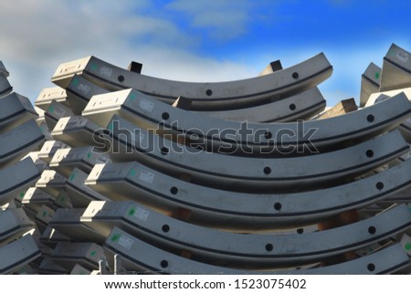 Pile of underground tunnel segments with blue sky background. The segments are pre cast, curved and interlock. They are being stored in tunnel manufacturing facility.