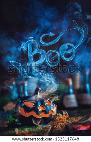 Halloween concept with a ceramic pumpkin and Boo lettering made out of the smoke. Creative autumn still life on a dark background
