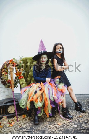 Two Asian girls wearing costume and boots. Children with face painting. Witch and skeleton kids. Rustic furniture in the outdoors. Antique clock. Black dress. Kids activity and fall photo shoot.