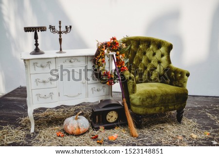 Halloween outdoor setting for photoshoot. Vintage white furniture and clock with green couch. Antique candle stand. Fall wreath. Witch broom. Hay on ground with fall leaves. Autumn in the outdoors.