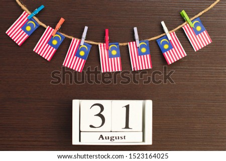 Flags of Malaysia hanging on clothesline attached with wooden clothespins and wooden calendar on wooden background. Concept independence day of Malaysia