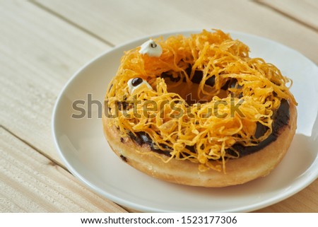 A plate of delicious yellow halloween doughnut in spider cartoon on wooden background
