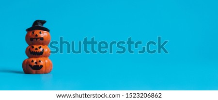Stock photo of Halloween pumpkin funny faces, jack o'lantern stacking on blue background. Fall autumn and Halloween Festival Concept. Crop in banner ratio with copy space.
