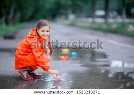 girl plays in paper boats in a puddle / autumn walk in the park, a child plays in the rain