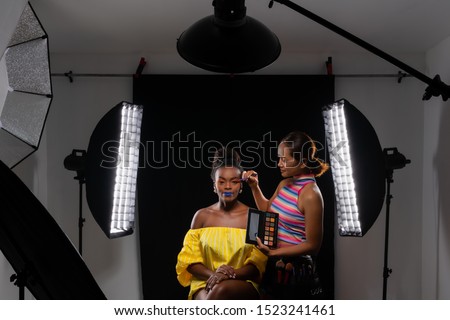 Professional make up artist working with african fashion model at photo studio with many equipment for photography. Light modifier, flash, Beauty Dish, Stripbox, Reflector. Royalty-Free Stock Photo #1523241461