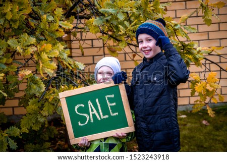 Two boys point to the inscription on the plate. Sign for advertising in the hands of children. The boys are happy and smiling. Autumn sales, discounts, cheap prices. Autumn came, yellow leaves.
