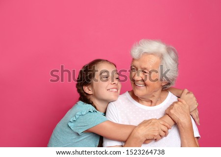 Cute girl hugging her grandmother on pink background