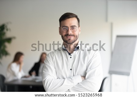 Confident happy young male manager in eyeglasses standing with folded hands head shot portrait. Smiling company owner, startup businessman, team leader, successful employee looking at camera. Royalty-Free Stock Photo #1523265968