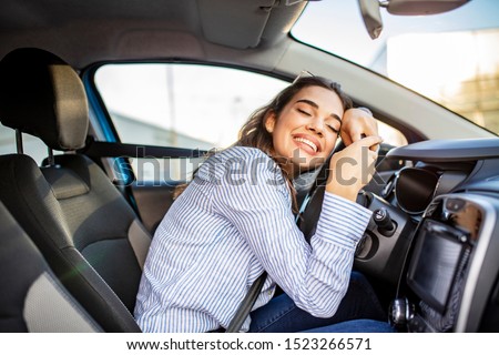 Young and cheerful woman enjoying new car hugging steering wheel sitting inside. Woman driving a new car. Woman Driver Portrait at Car