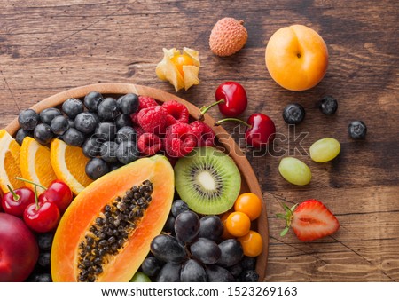 Fresh raw organic summer berries and exotic fruits in round wooden plate on wooden kitchen background. Papaya, grapes, nectarine, orange, raspberry, kiwi, strawberry, lychees, cherry.Top view Royalty-Free Stock Photo #1523269163