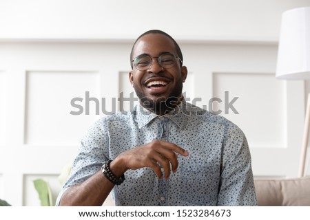 Close up head shot portrait of happy african american man in eyeglasses looking at camera, young smiling black male blogger influencer recording video, talking, laughing, having fun at home.