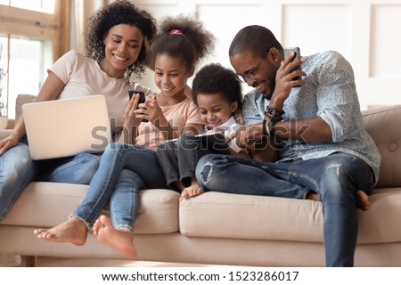 Obsessed to tech devices happy african american family using digital tablet, computer, smartphones. Smiling dad teaching son to use gadgets while mom watching daughter posting in social networks. Royalty-Free Stock Photo #1523286017