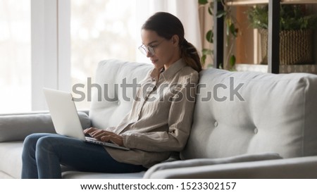 Serious focused young woman freelancer working on freelance from home typing email on laptop, girl student using computer for study online course sitting on couch busy on distance internet job