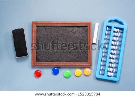 Blackboard frame with copy space, color magnets, chalk with sponge on blue flat lay background. Back to school concept.